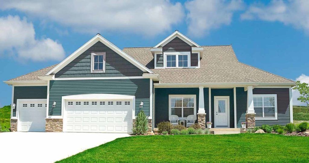 A modern, dark-sided suburban home with a multi-car garage, white trim, and stone accents, set against a bright blue sky.