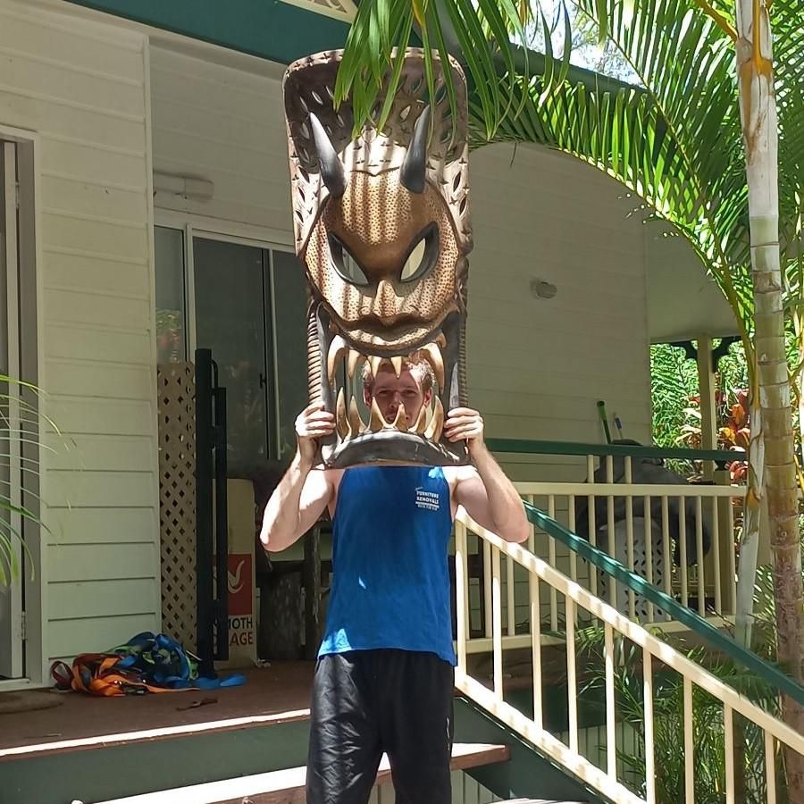 Man Holding Large, Carved Wooden Mask Above His Head Outdoors — John's Furniture Removals in Hervey Bay, QLD