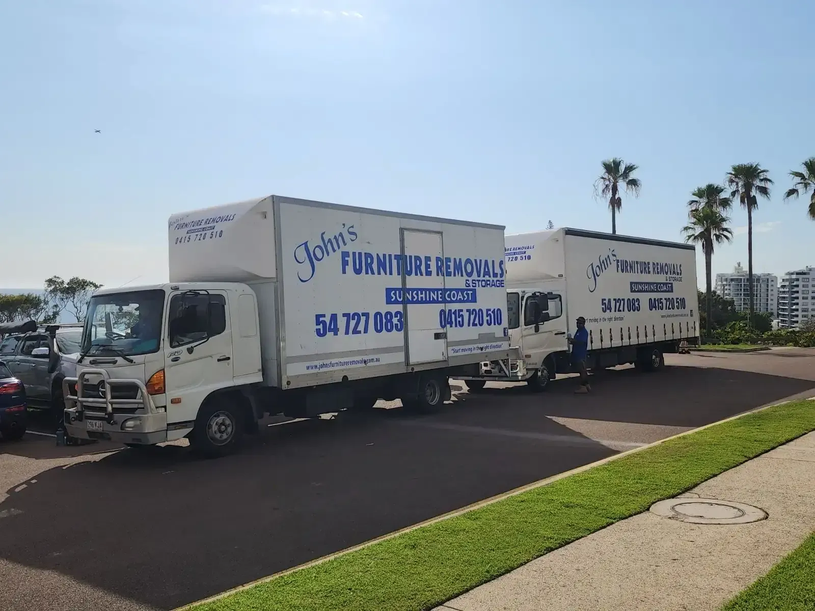 Two White Moving Trucks Parked on a Road With Palm Trees in the Background — John's Furniture Removals in Sunshine Coast, QLD