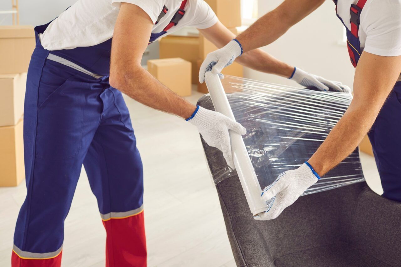 Two Movers in Blue Overalls Wrapping Furniture With Plastic Wrap — John's Furniture Removals in Gold Coast, QLD