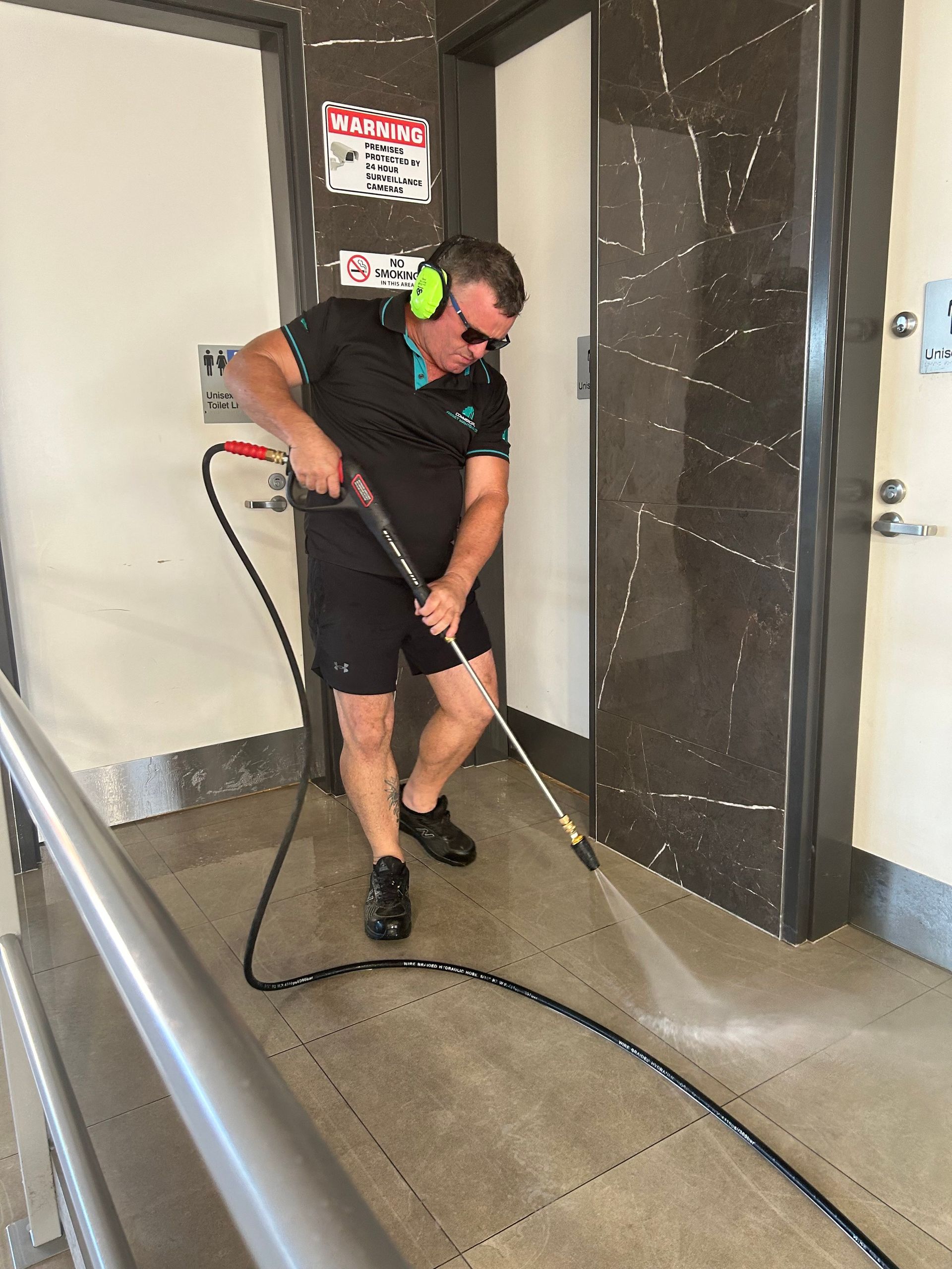 A Man Washing a Hallway Floor with A Pressure Washer — Commercial Asset Maintenance In Logan, QLD