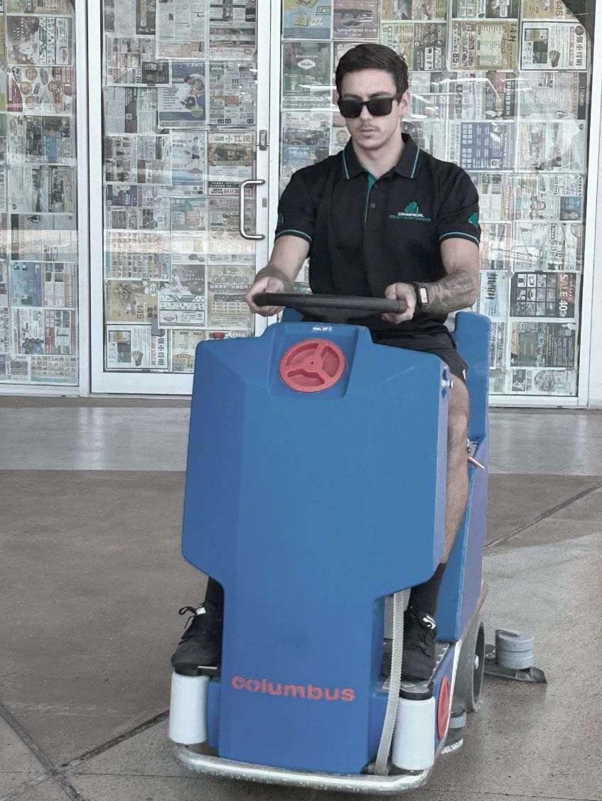 A Man is Cleaning a Tiled Floor With a Yellow Machine — Commercial Asset Maintenance In Yandina, QLD