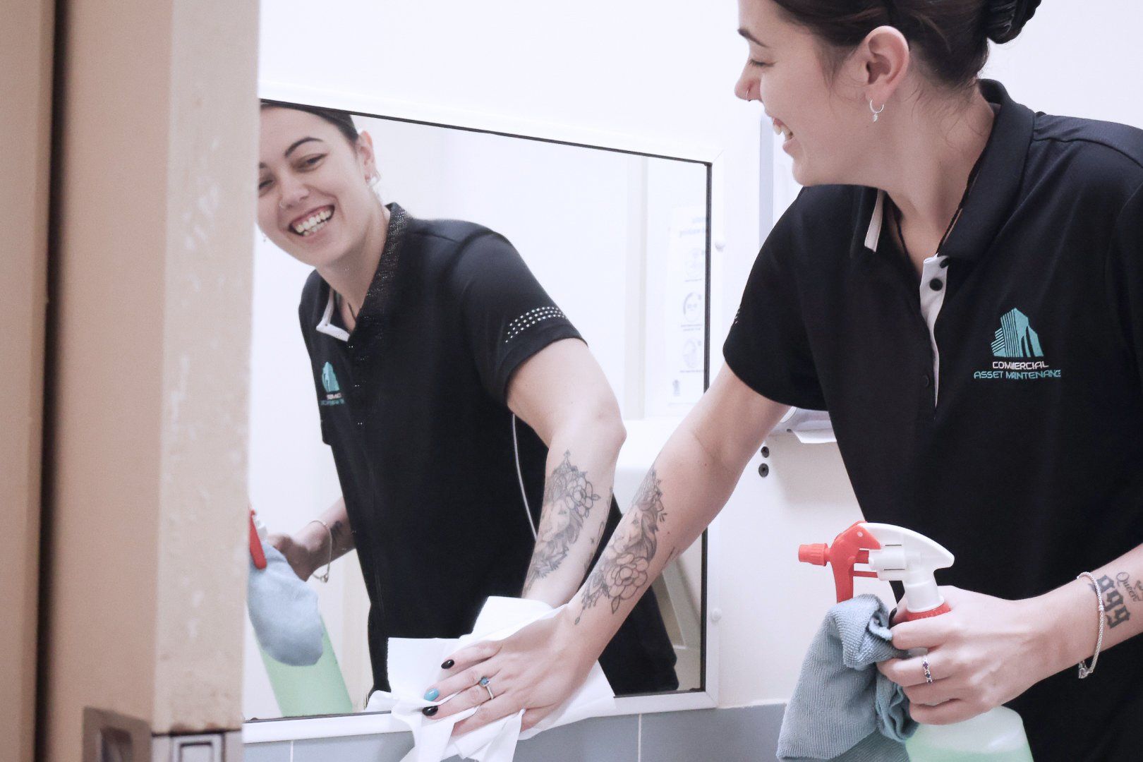 A Woman Cleaning a Mirror in A Bathroom — Commercial Asset Maintenance In Burpengary, QLD