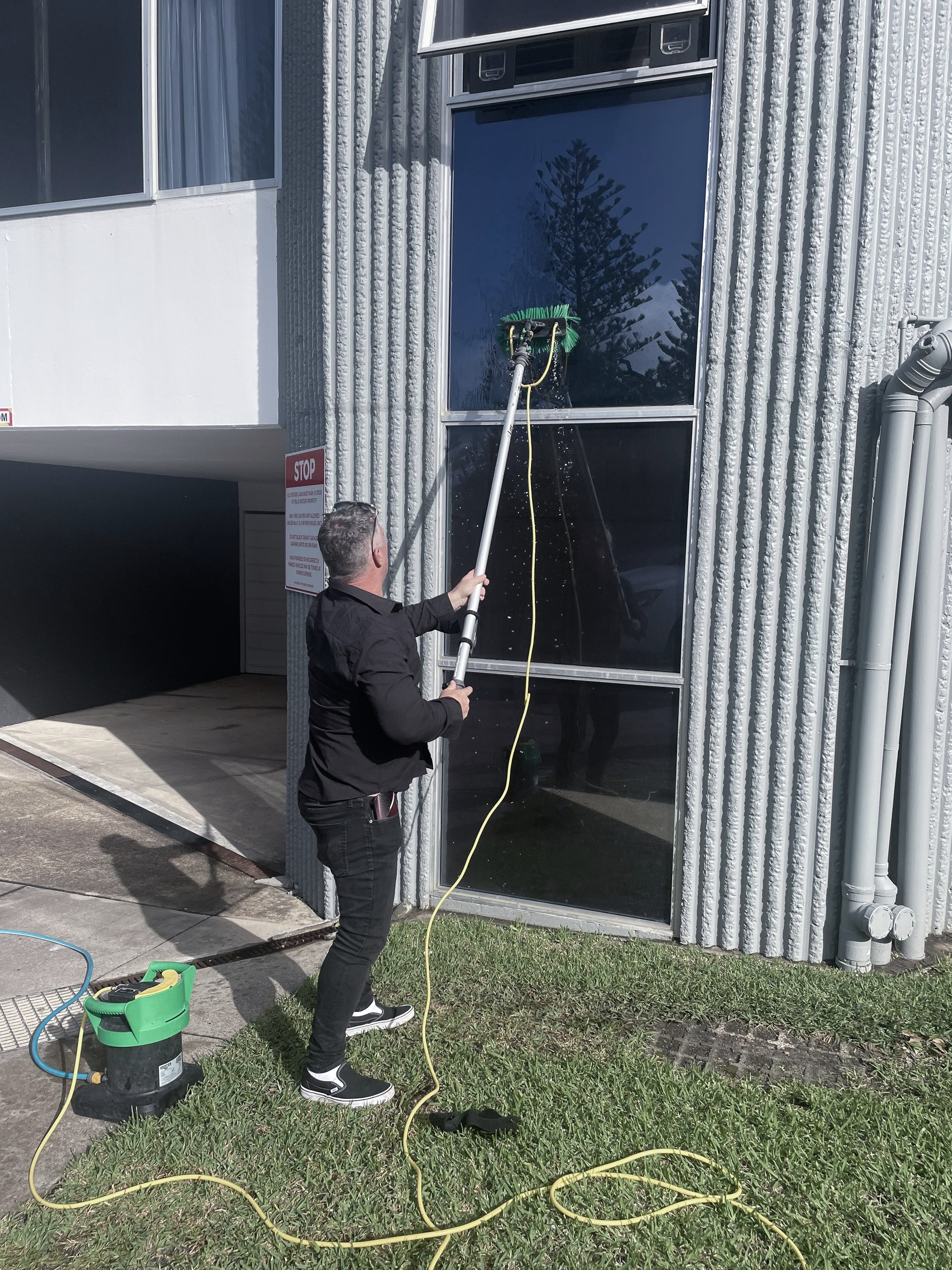 A Man Cleaning a Tall Window on A Building — Commercial Asset Maintenance In Bribie Island, QLD