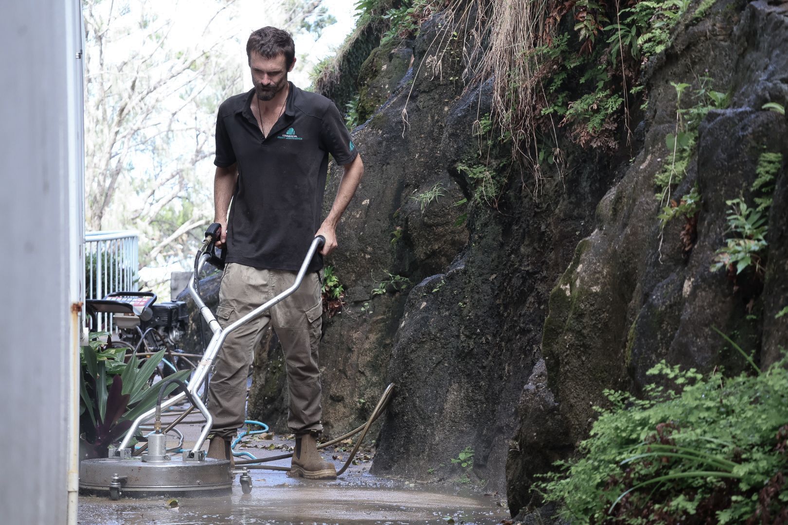 A Man is Standing Next to a Bush Holding a Camera — Commercial Asset Maintenance In Coolum Beach, QLD
