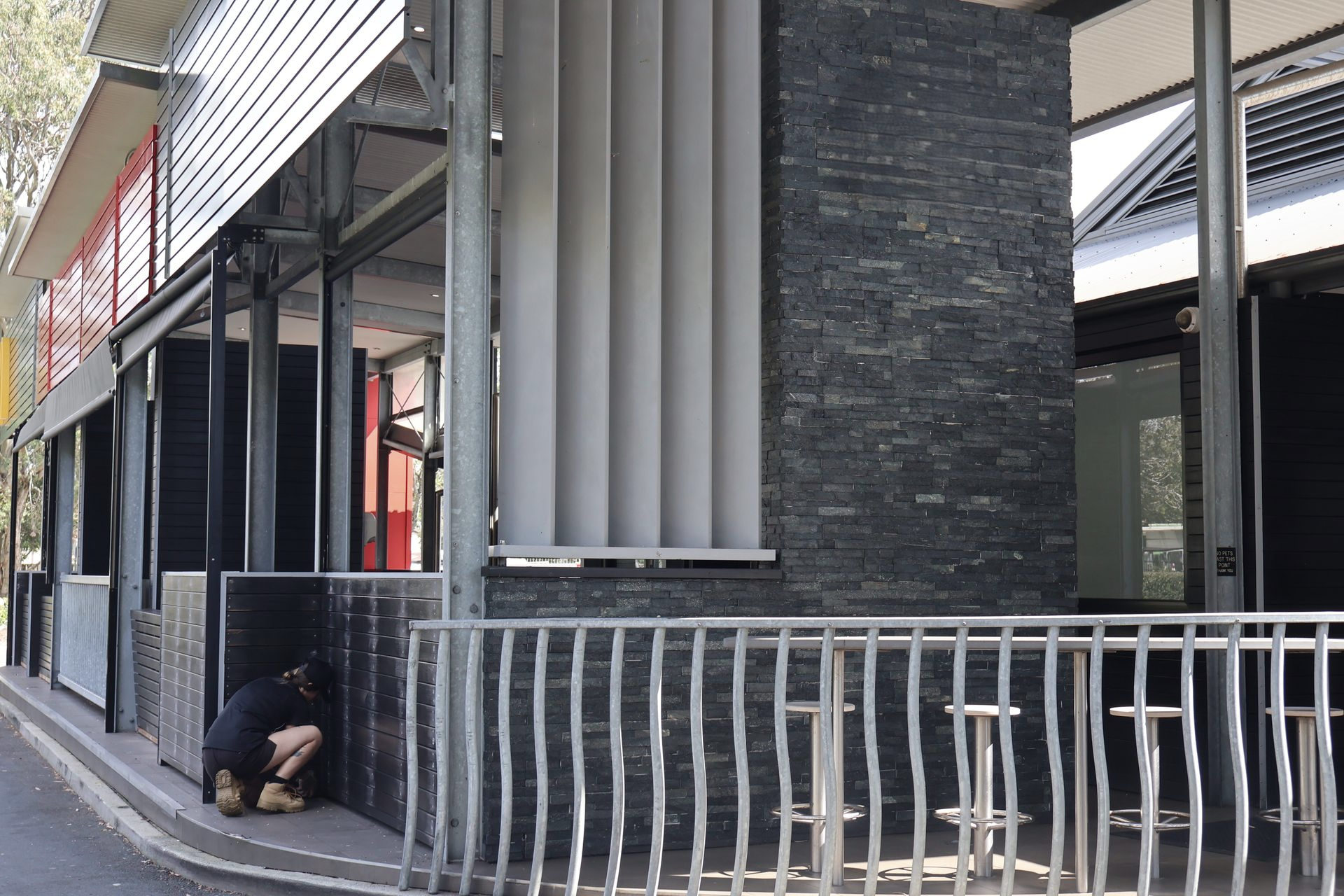 A Person Crouches Beside a Dark Brick Building — Commercial Asset Maintenance In Strathpine, QLD