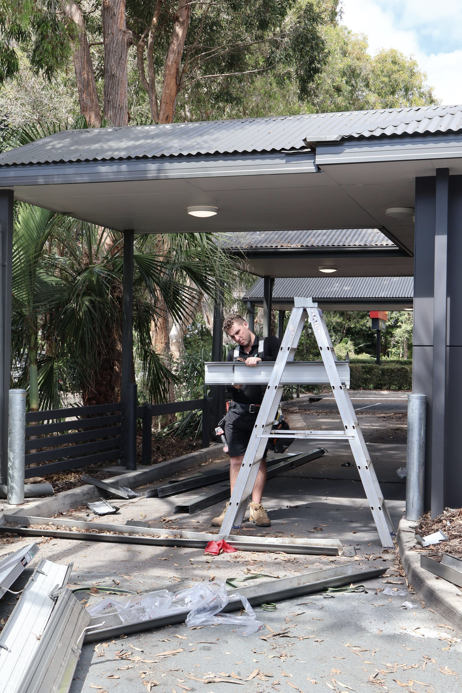 A Man on A Ladder Repairs a Drive-Through Canopy — Commercial Asset Maintenance In Coolum Beach, QLD