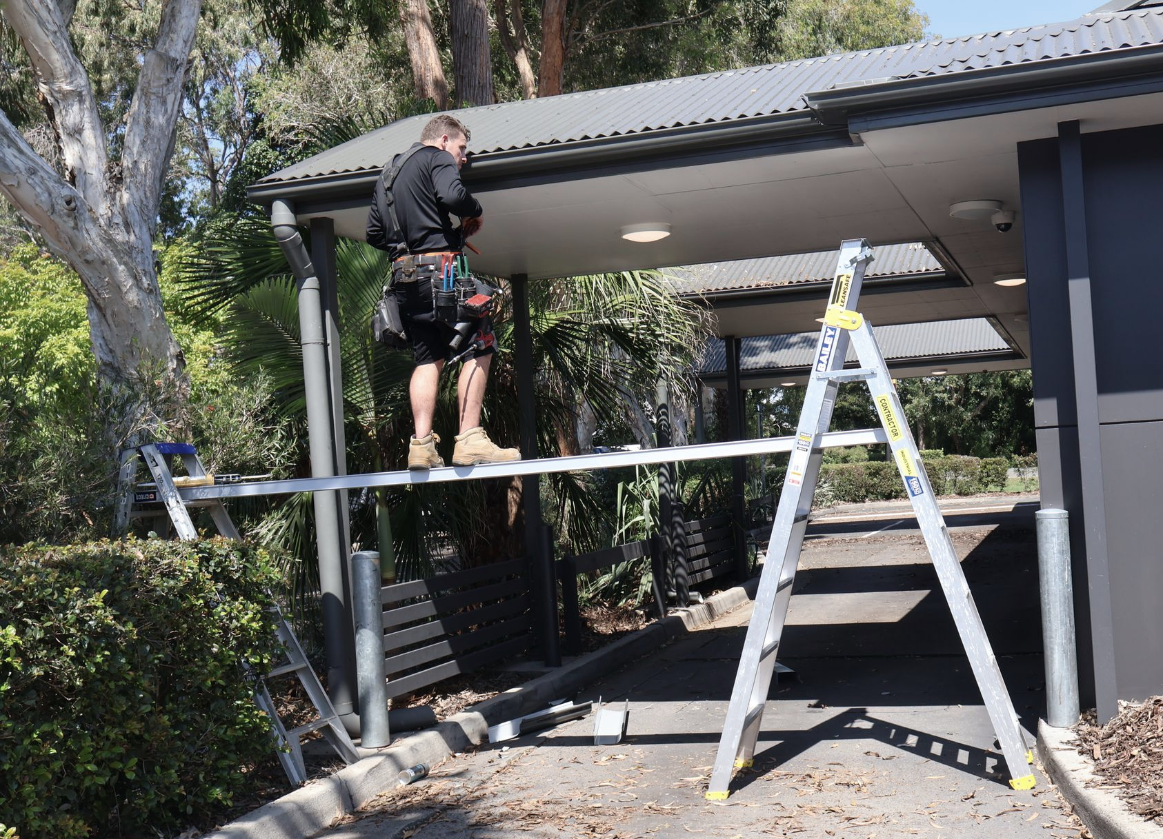 A Man on A Scaffold Working on A Building Roof — Commercial Asset Maintenance In Logan, QLD