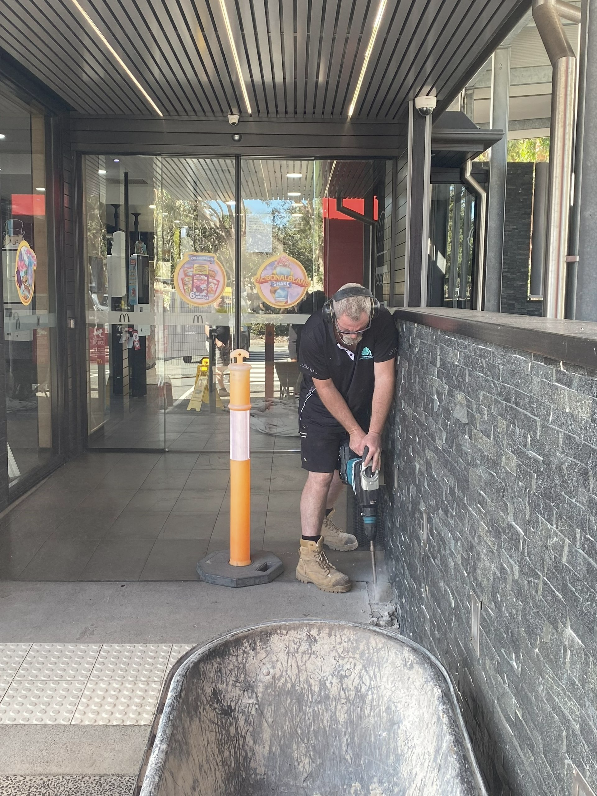 A Man Using a Drill to Work on A Wall Outdoors — Commercial Asset Maintenance In Brisbane, QLD