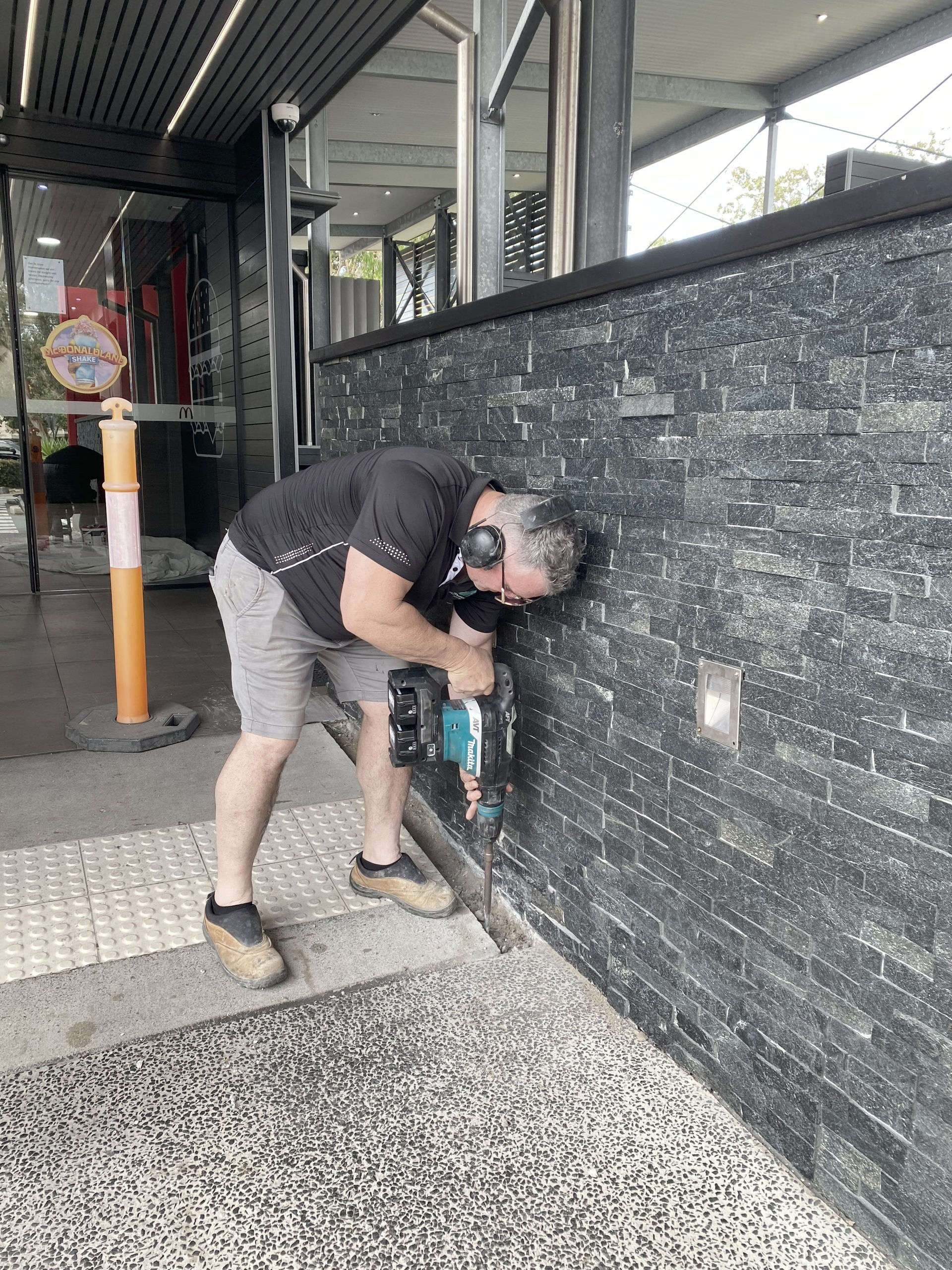 A Man Using Power Tool on Dark Brick Wall  — Commercial Asset Maintenance In Morayfield, QLD