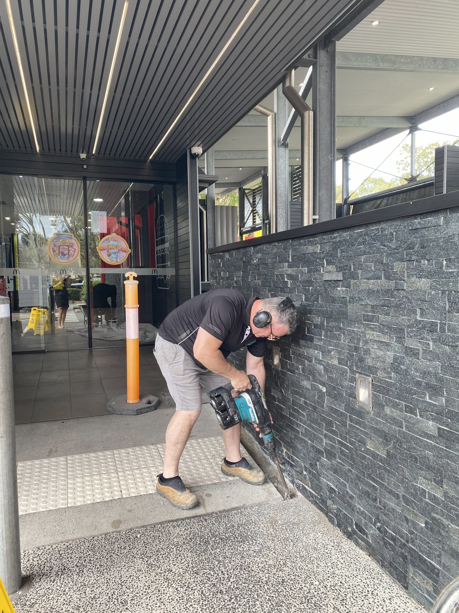 A Man Using a Jackhammer on A Dark Brick Wall Outdoors — Commercial Asset Maintenance In Redcliffe, QLD