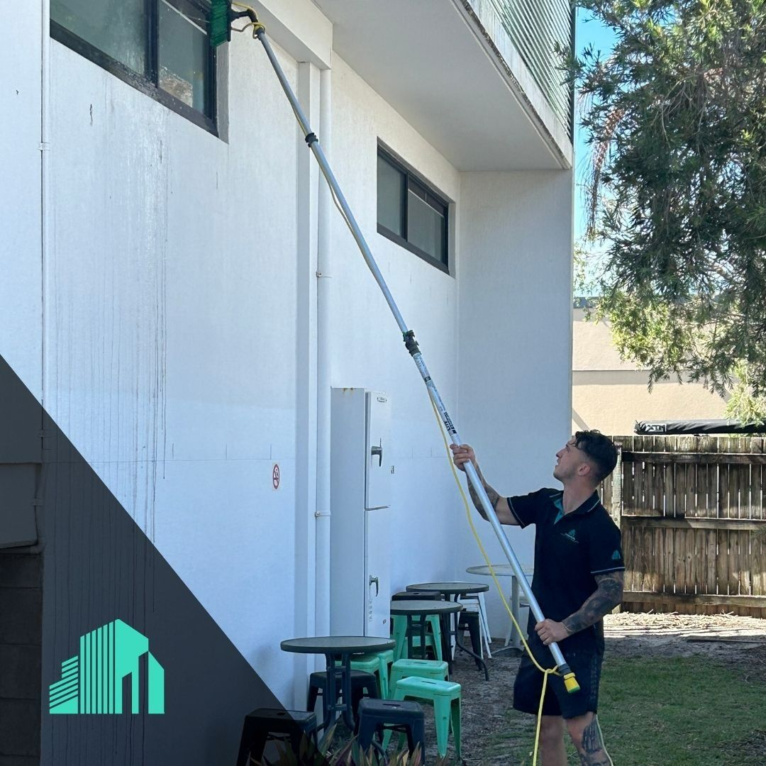 A Man Washing Building Wall with Long Pole — Commercial Asset Maintenance In Burpengary, QLD