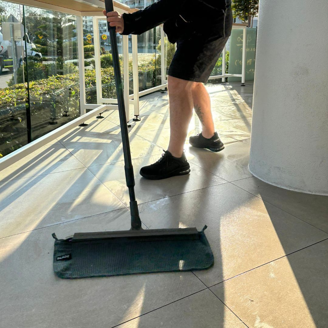 A Person Mopping a Tiled Balcony Floor — Commercial Asset Maintenance In Caloundra, QLD