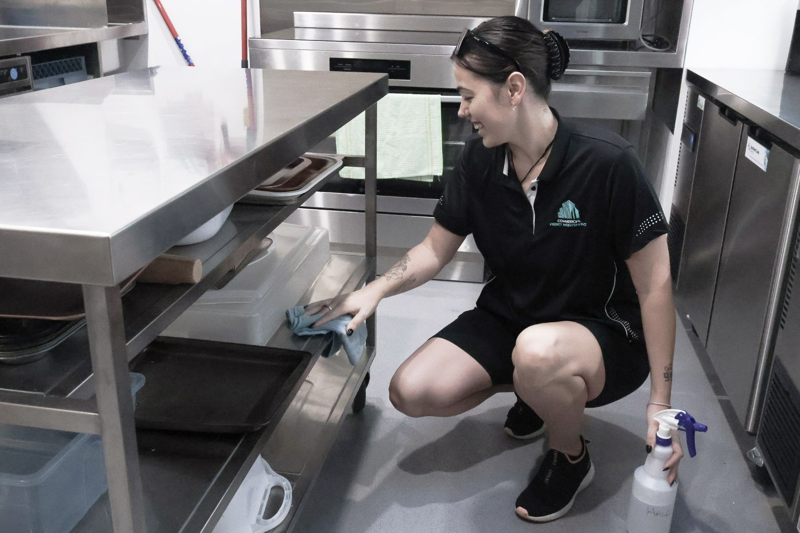 A Woman Cleaning Stainless Steel Shelf in A Commercial Kitchen — Commercial Asset Maintenance In Yandina, QLD