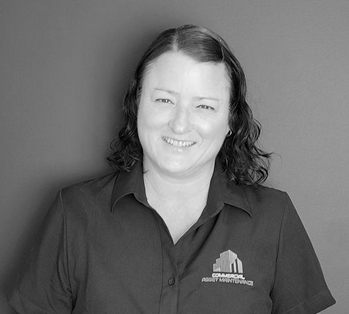 Woman smiling, wearing a dark collared shirt with a company logo, in front of a dark background. — Commercial Asset Maintenance In 1Gympie, QLD