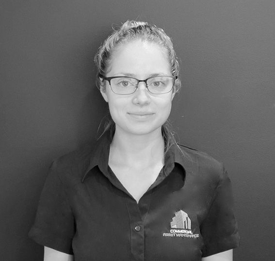 Woman with glasses wearing a button-up shirt with logo, standing in front of a dark wall. — Commercial Asset Maintenance In 1Gympie, QLD