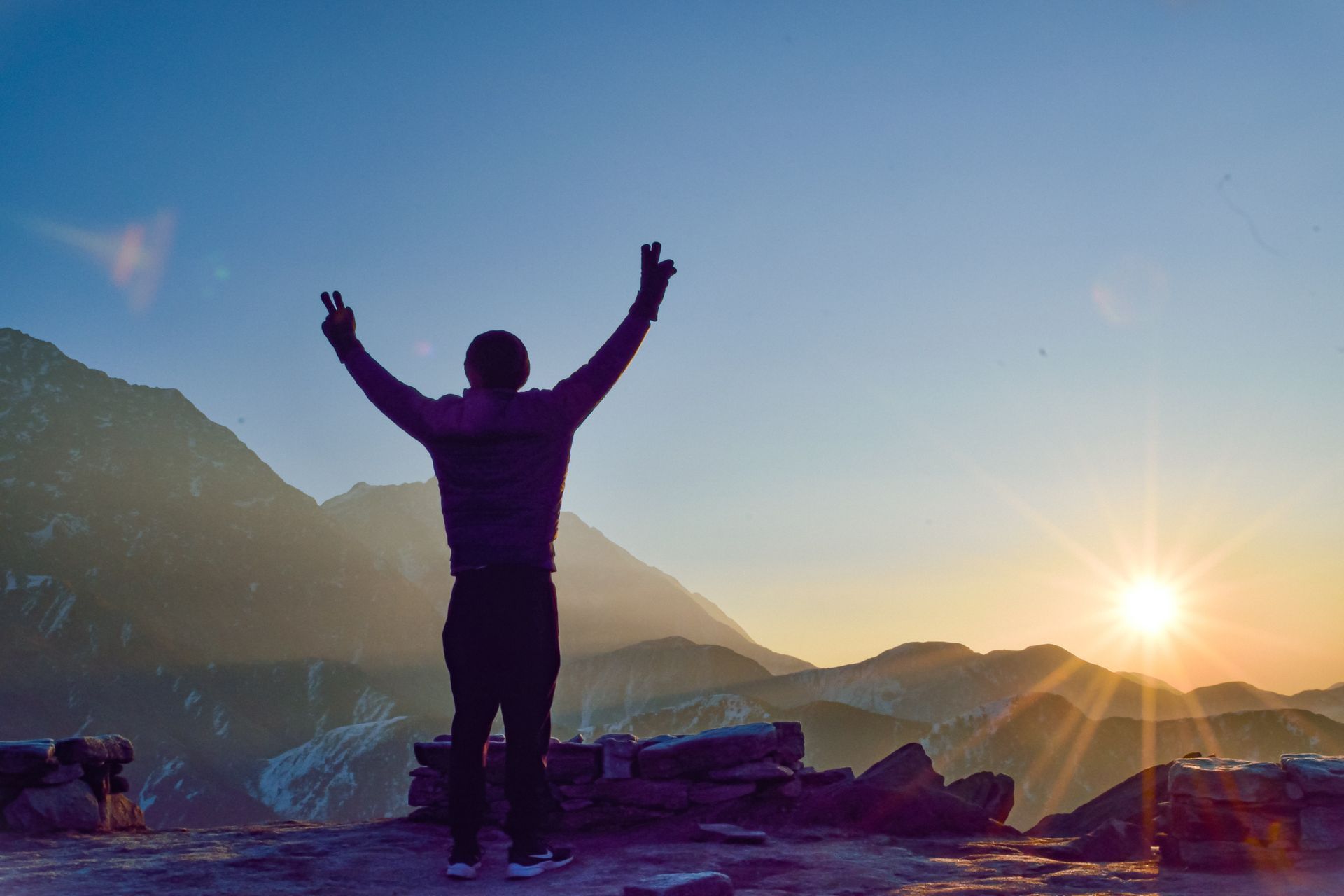 Person raising both arms on a mountain summit at sunrise