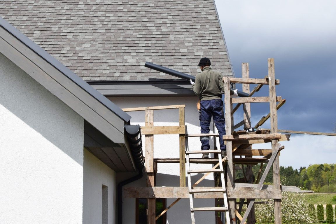 Worker on scaffolding painting a house roof edge with a roller