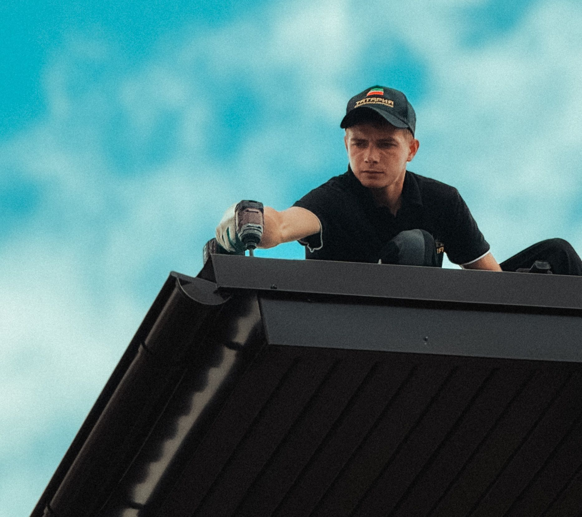 Worker on a rooftop using a tool against a bright blue sky