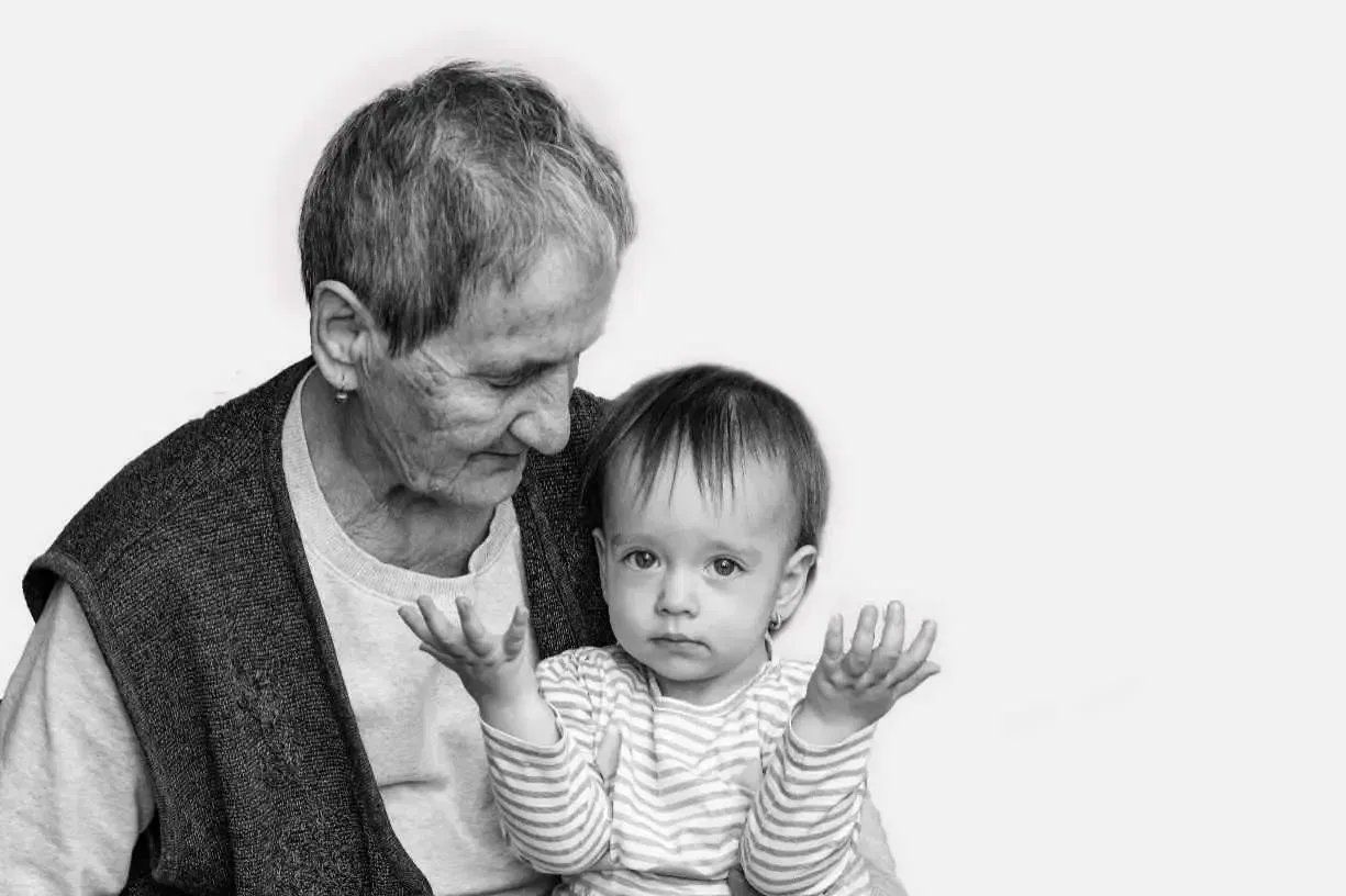 An elderly woman is holding a baby in her arms in a black and white photo.
