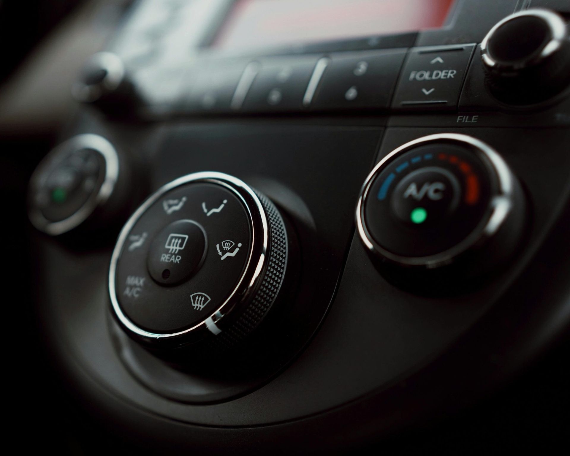 Car dashboard: Climate control knobs, buttons, and display. Black with silver accents.