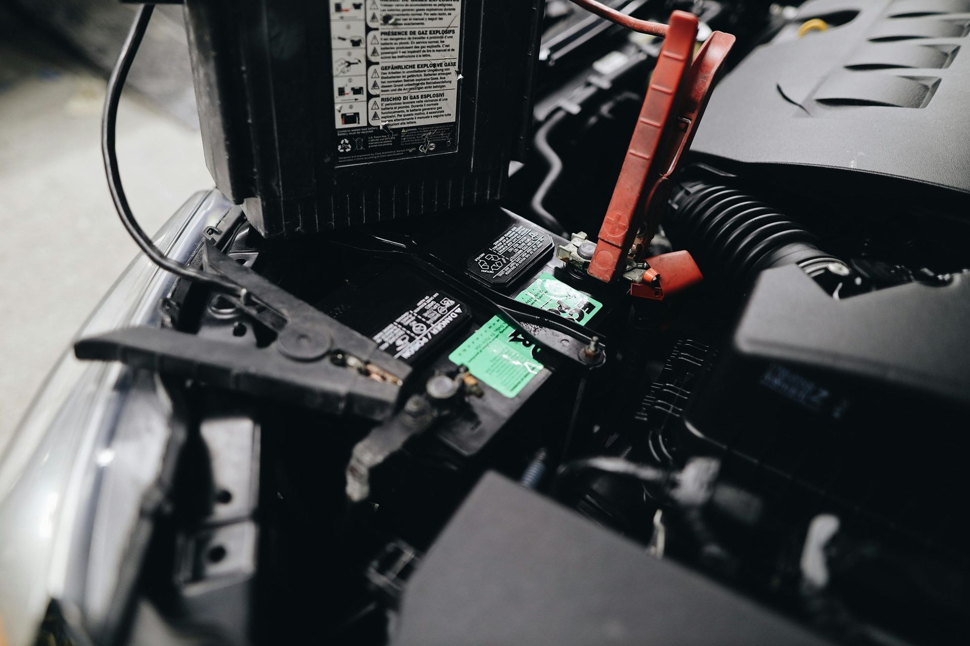 Car battery being jump-started with jumper cables connected to a battery under the open hood.