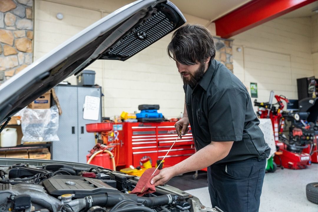 Mechanic checking oil level in car engine, inside a garage.