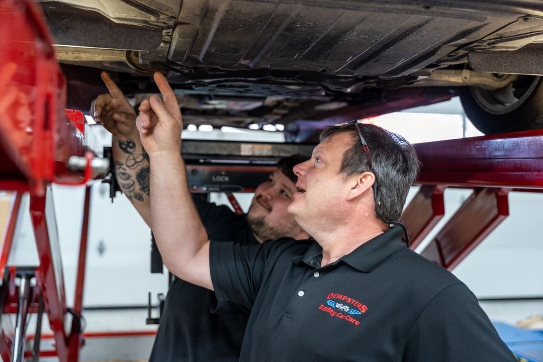 Two mechanics examining the underside of a car on a lift; one points up.