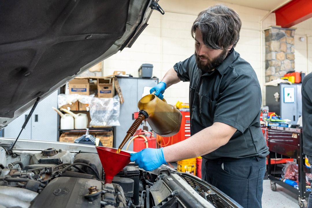 Mechanic pouring oil into a car engine, wearing gloves.