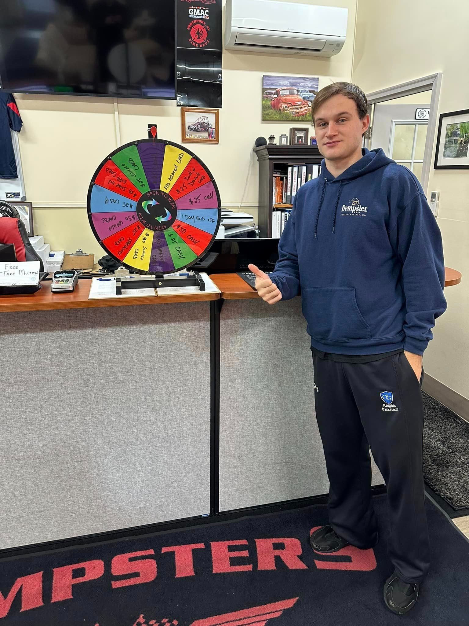 Man beside colorful prize wheel in an office setting. He is giving a thumbs up.