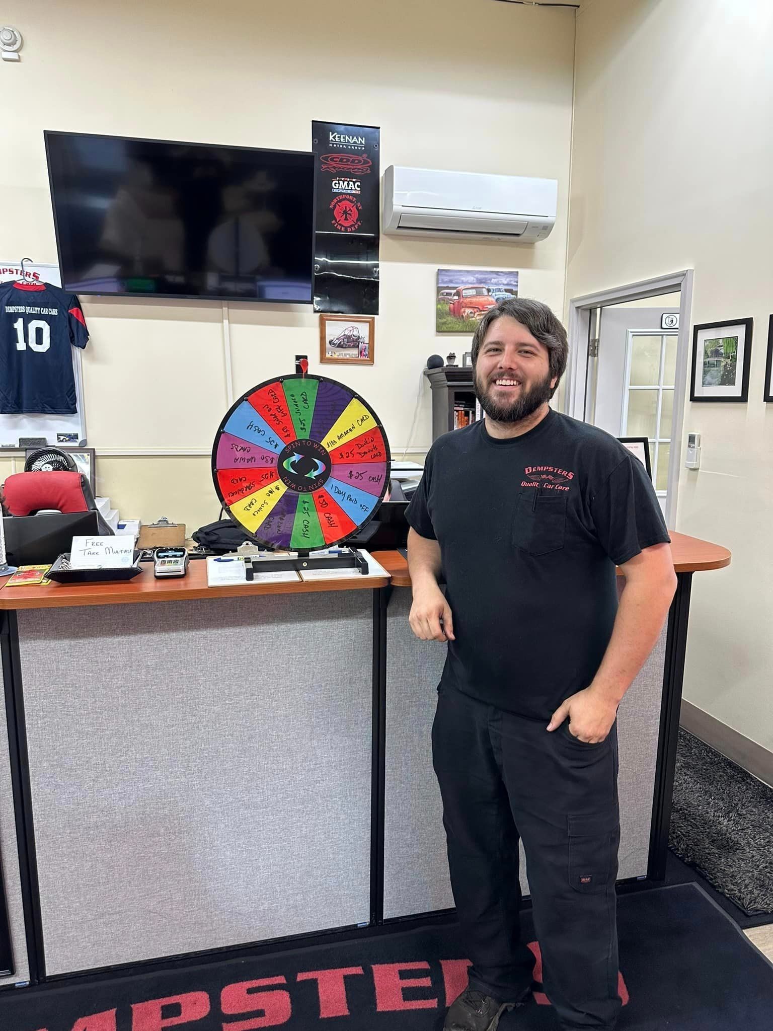 Man stands near a prize wheel at a business counter, smiling.