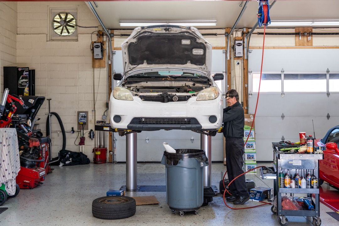 Mechanic working on car raised on a lift inside a garage, hood open.