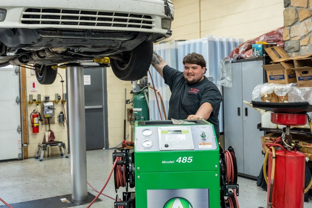 Mechanic working under a car on a lift. He is smiling and operating a green machine in a garage.
