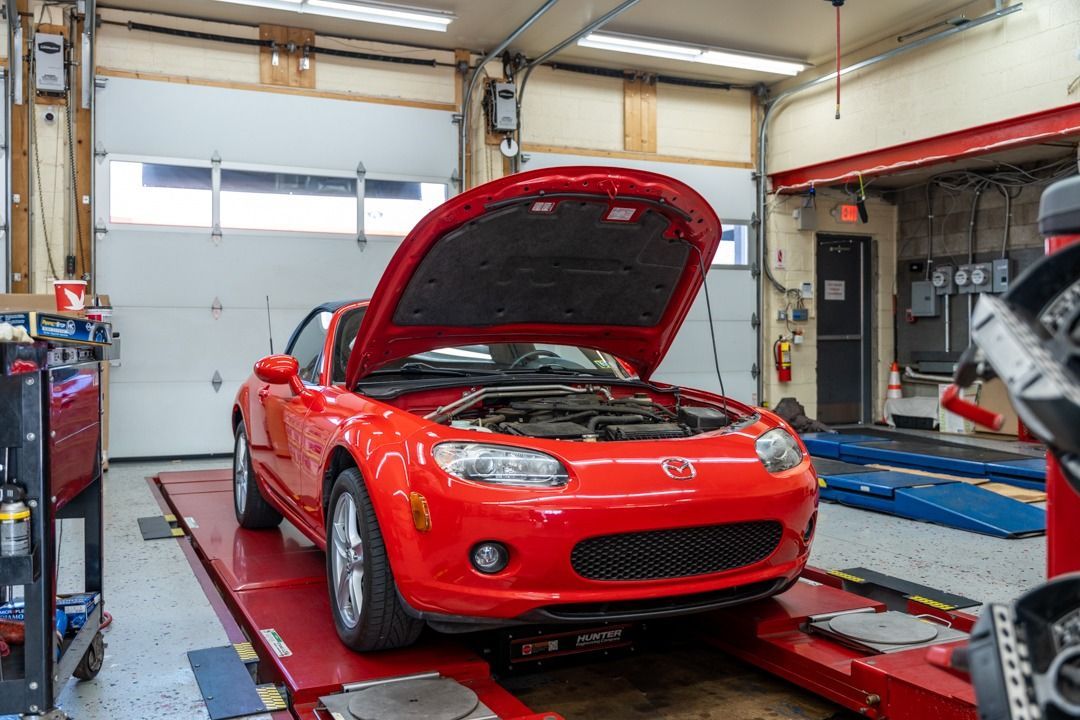 Red convertible car with hood open in a repair shop, on a lift.