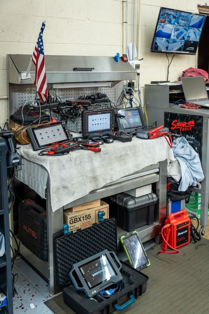 Workbench in a garage with diagnostic equipment, tools, and a security monitor. An American flag is displayed.