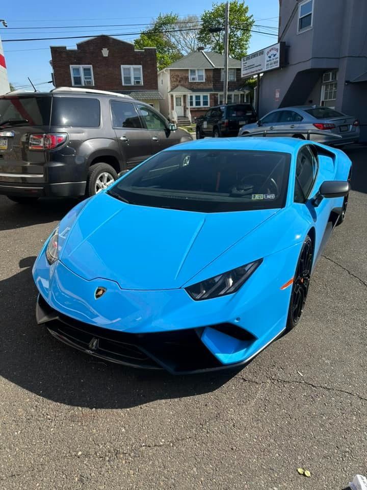 Blue Lamborghini sports car parked on a paved lot on a sunny day.