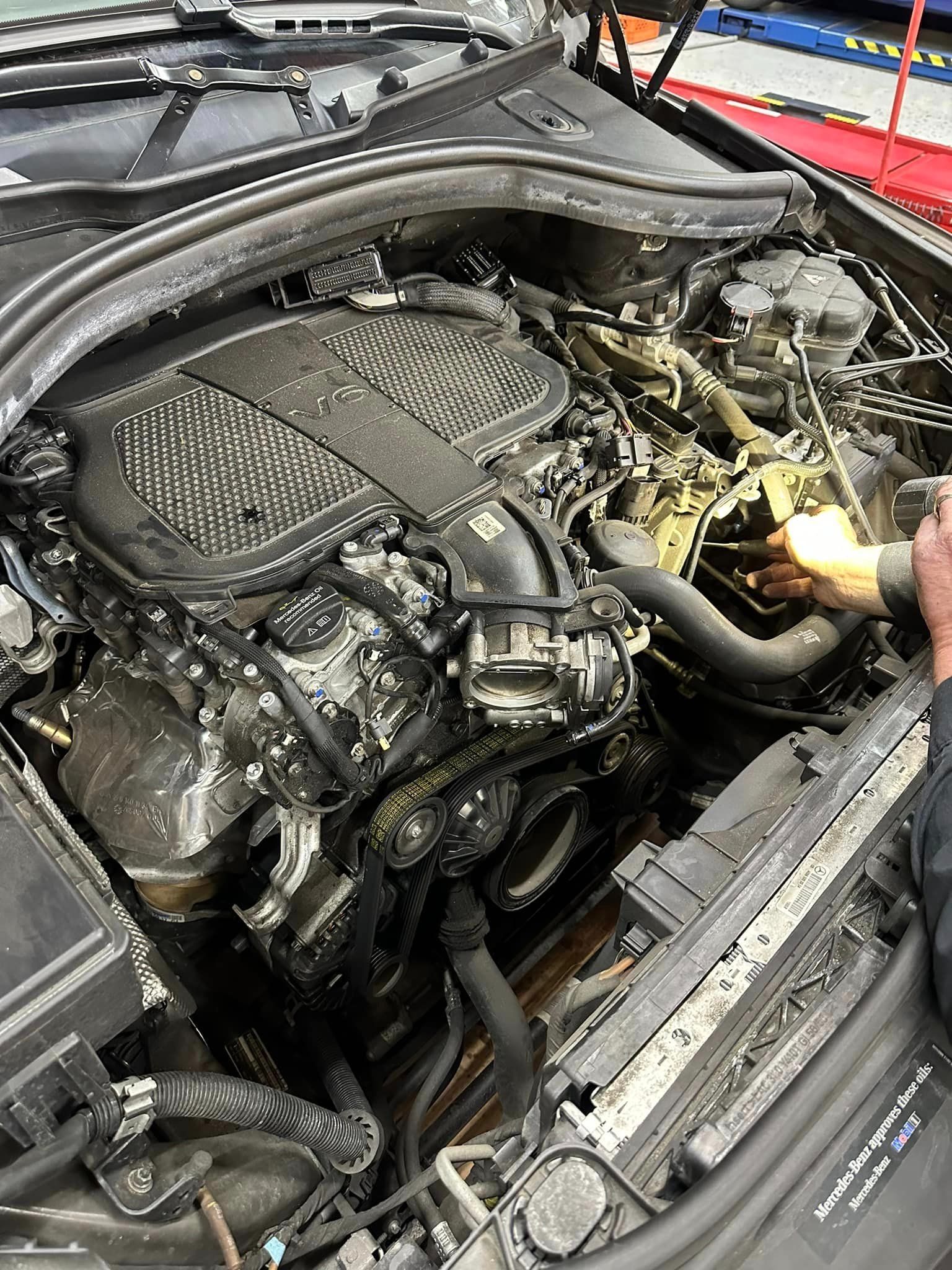 Engine compartment, possibly damaged. A mechanic's gloved hand reaches toward the engine.