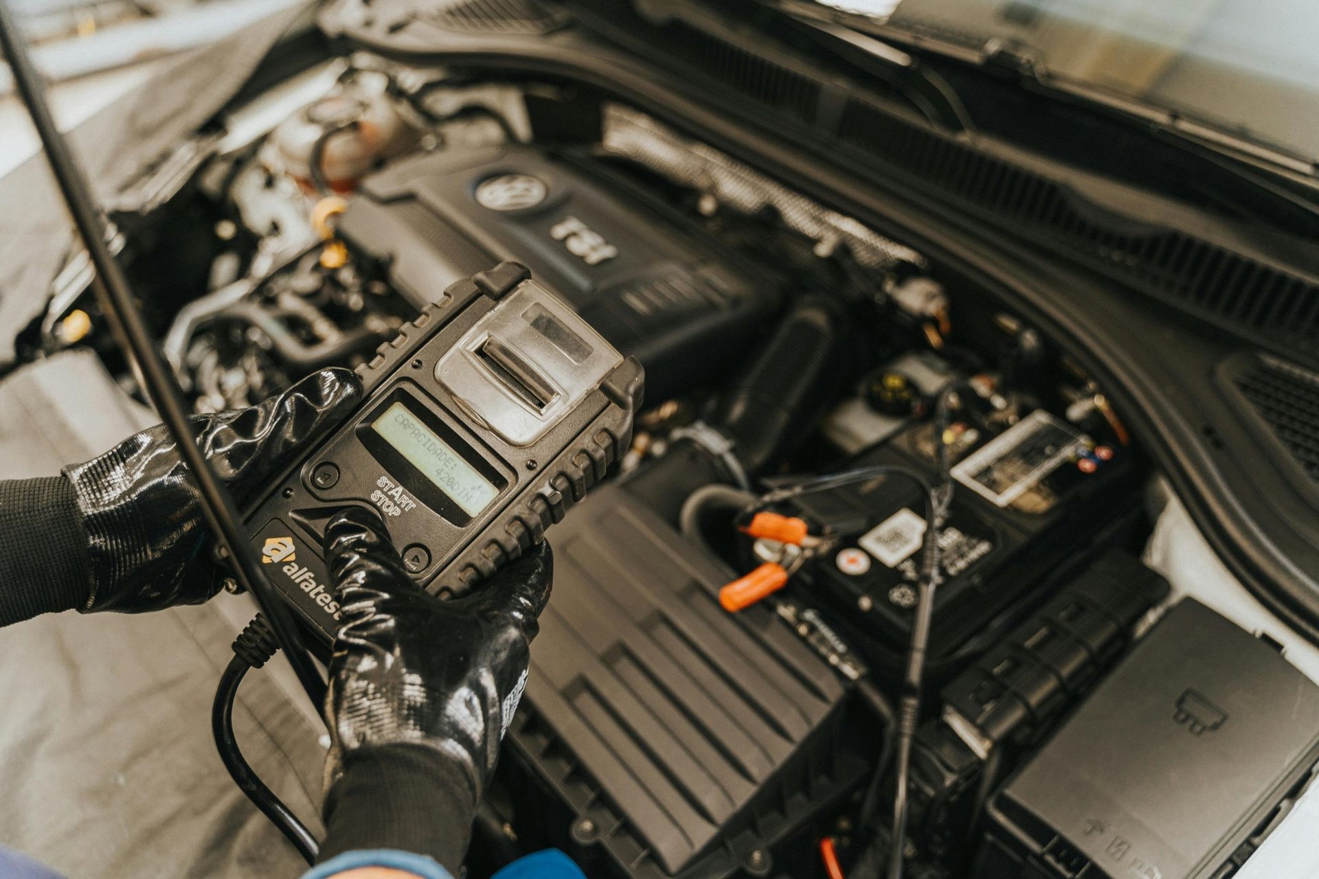 Mechanic using a diagnostic tool on a car engine in a garage setting.
