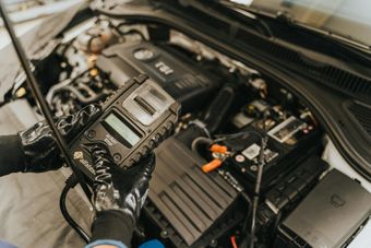 Hands in gloves holding a diagnostic tool over a car engine.