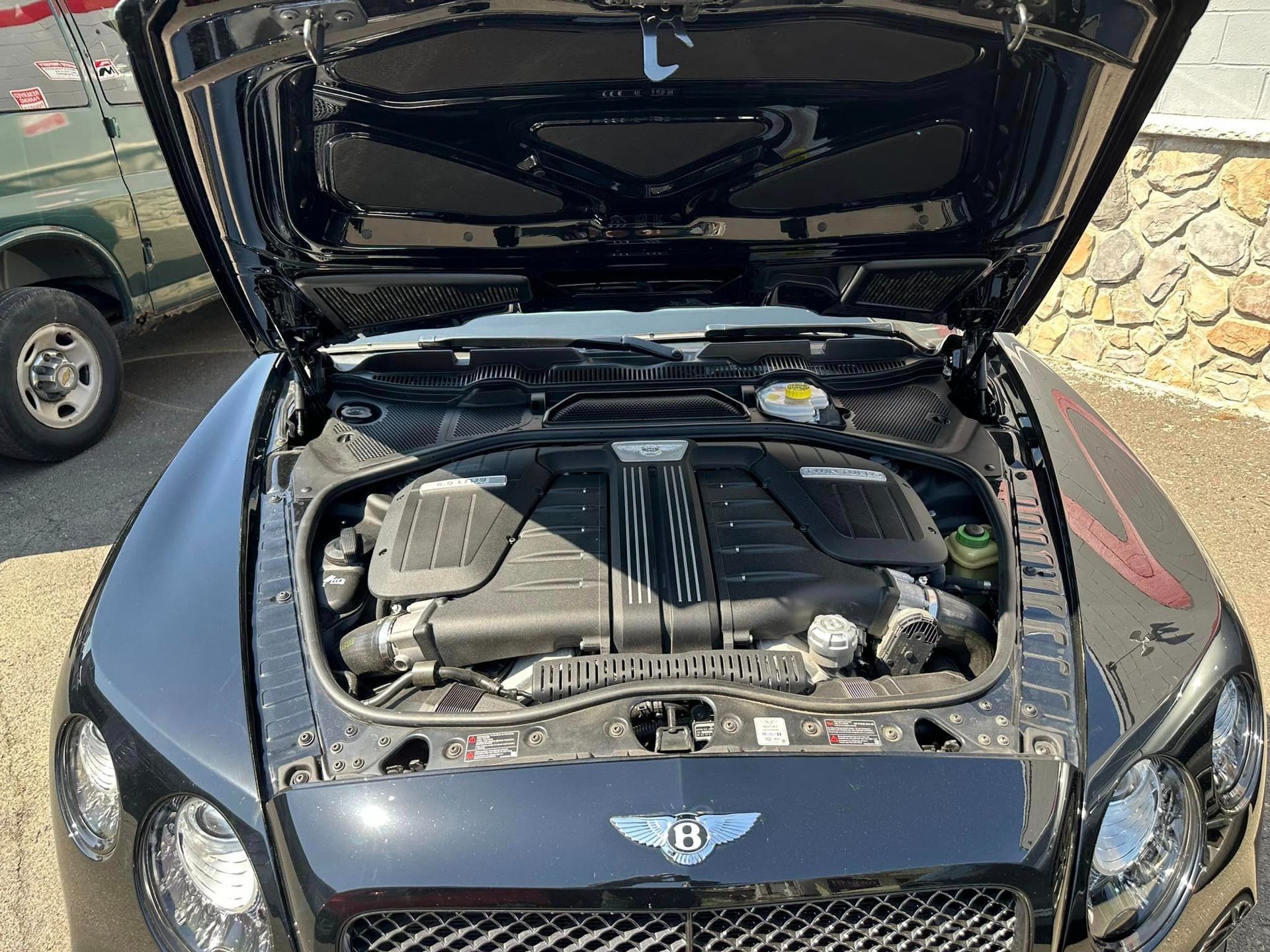 Black Bentley car hood open, engine bay visible.