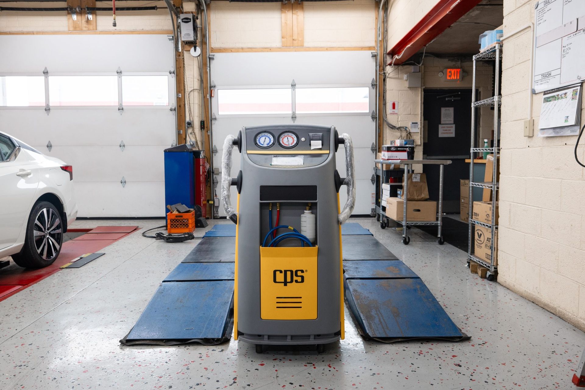 A car repair shop with an A/C servicing machine, a car, and service equipment.