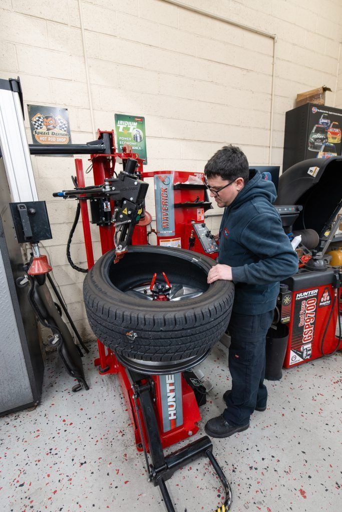 Person with glasses working on a tire using a red machine in a shop.
