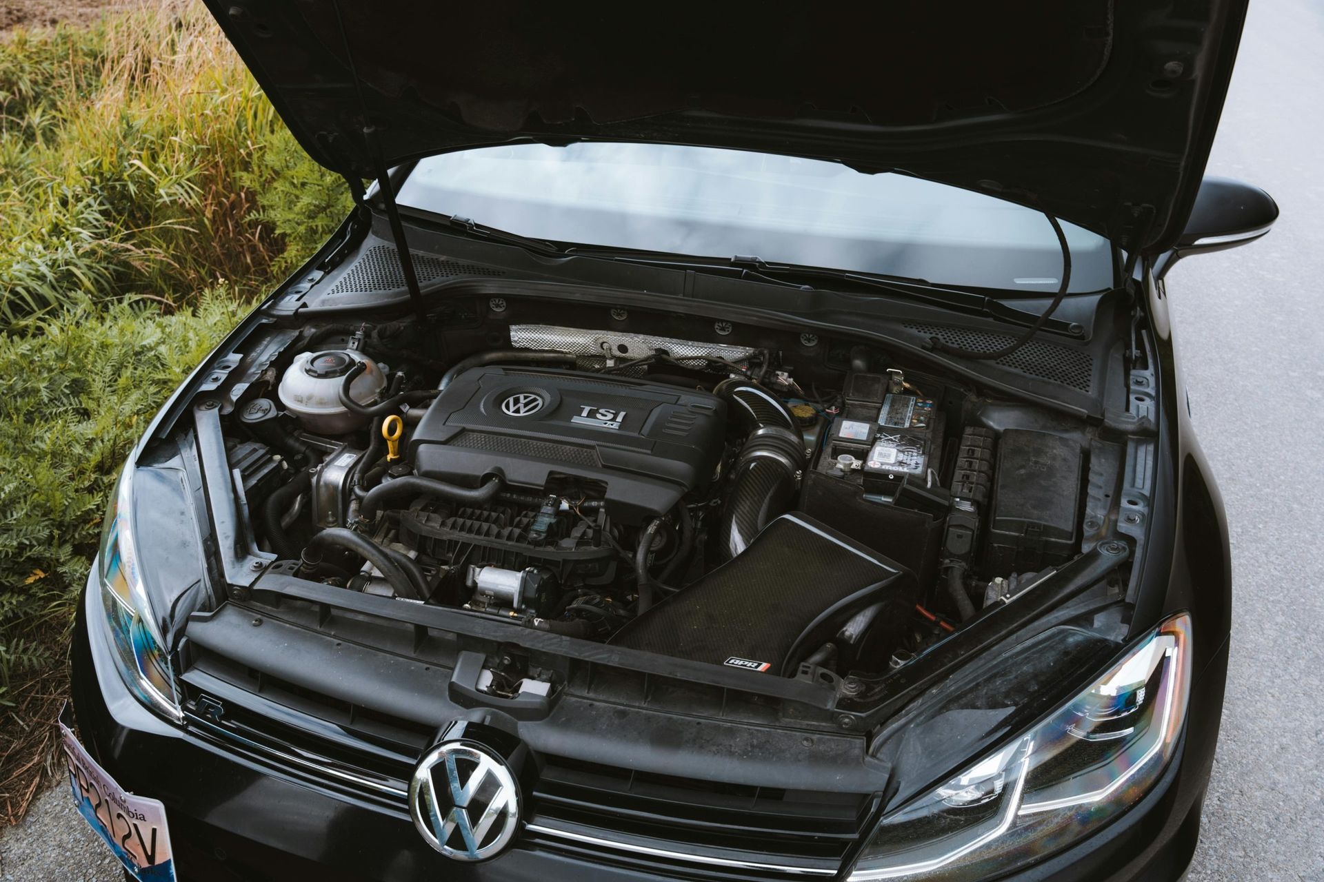 Black Volkswagen Golf GTI with hood open, showing the engine bay. Car is parked outdoors.