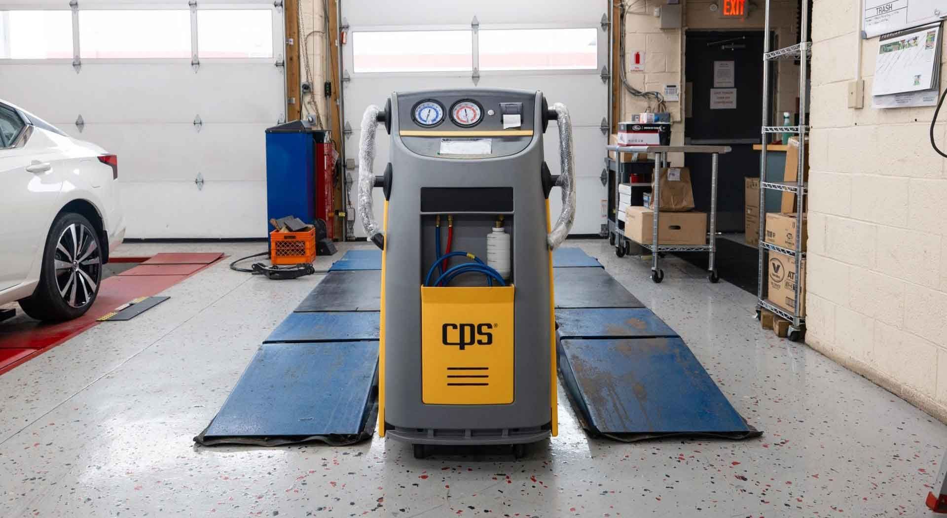 A car service machine in a garage setting with a car on a lift. The machine is gray and yellow.