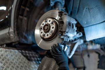 Mechanic in black gloves working on a car brake disc in a garage.