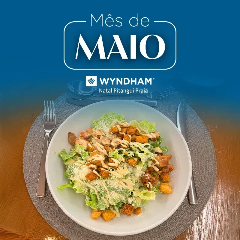 Prato de salada com molho, talheres e texto promocional “Mês de Maio” do Wyndham Natal Ponta Negra