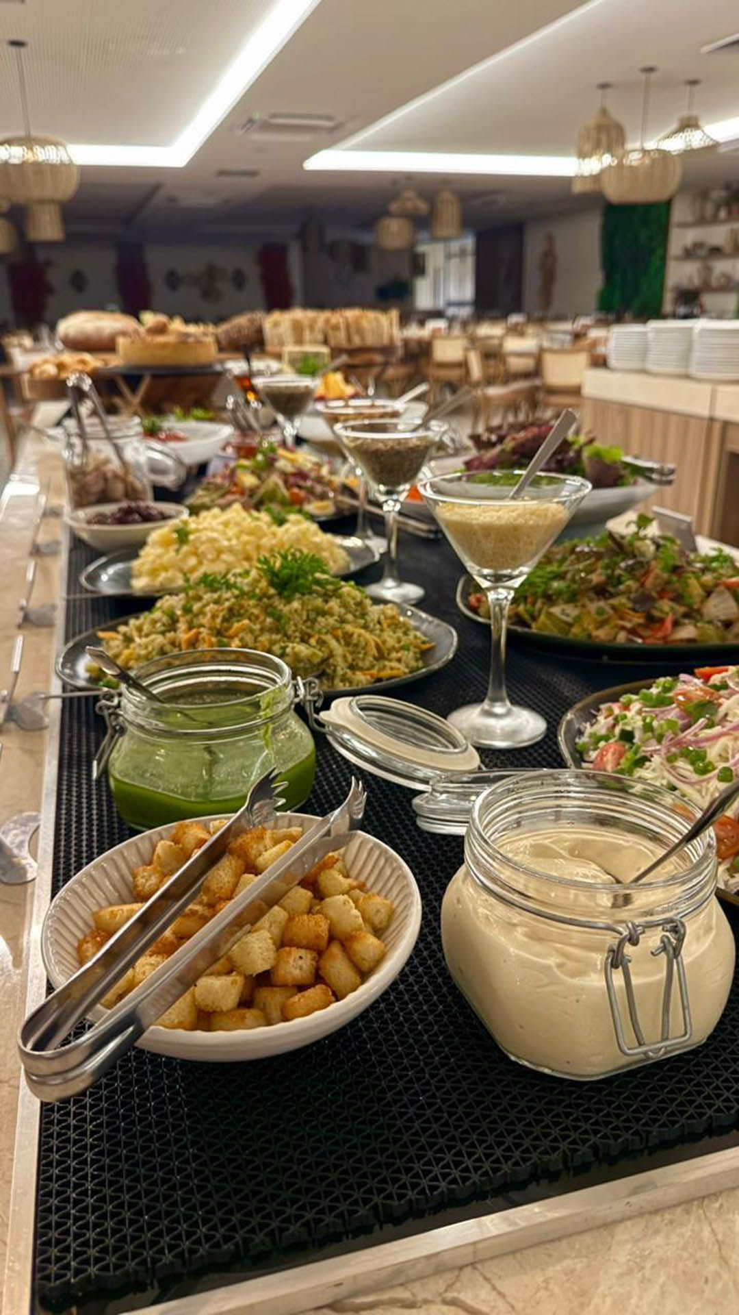 Mesa de bufê com saladas, aperitivos e sobremesas em tigelas e travessas de vidro.