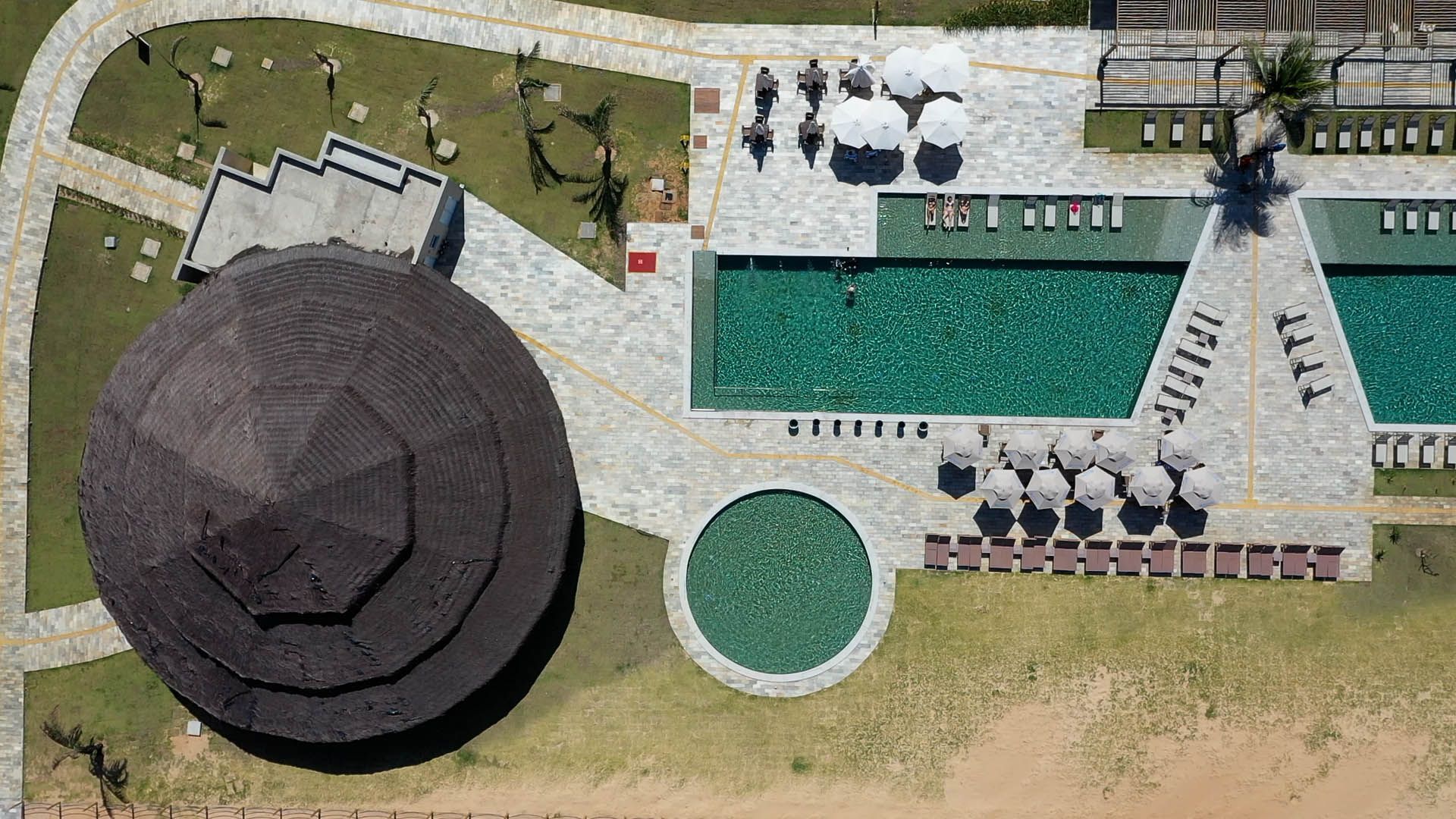 Vista aérea de um parque com uma grande cúpula escura, piscina retangular verde, piscina circular, caminhos e árvores.