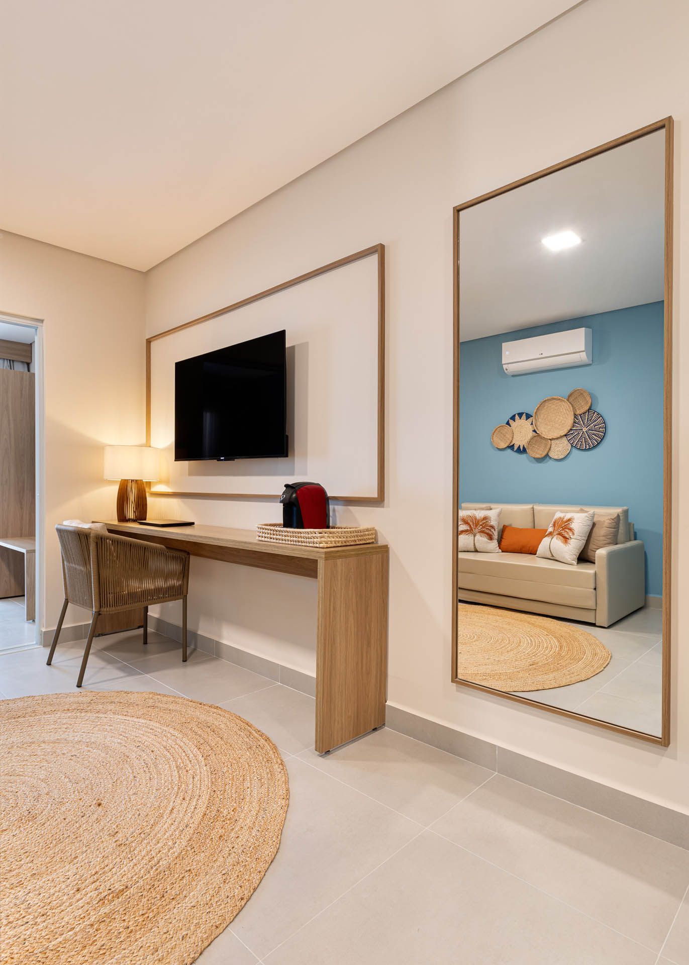 Sala de estar moderna com TV de parede, escrivaninha, espelho de chão e decoração em madeira clara com uma parede de destaque azul.