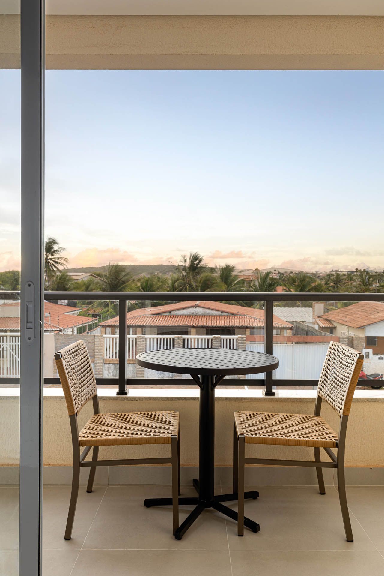 Mesa de varanda com duas cadeiras de vime e uma pequena mesa com vista para os telhados ao pôr do sol.